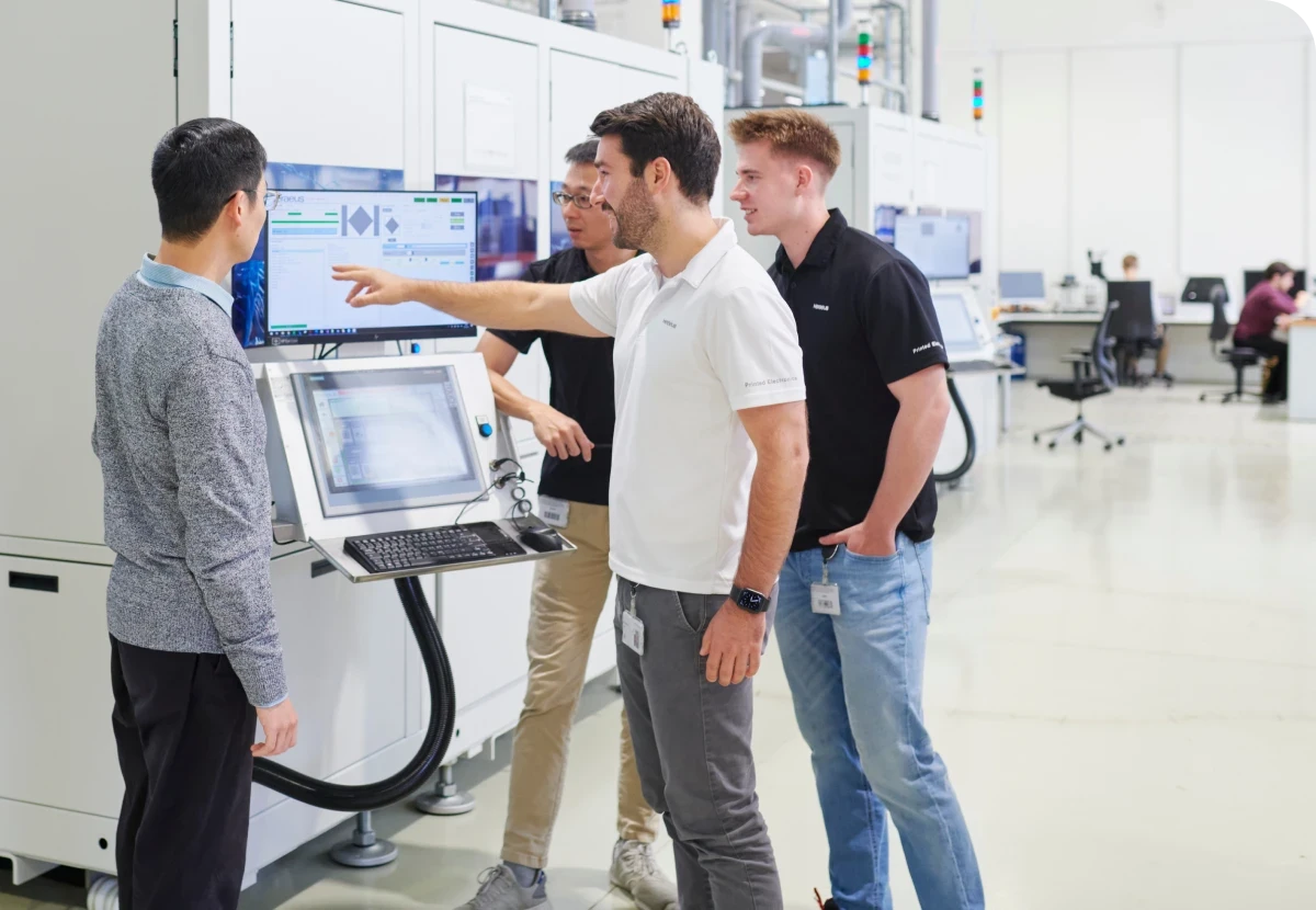 Four people in a tech lab discuss data displayed on a monitor. One person points at the screen, while others observe attentively.