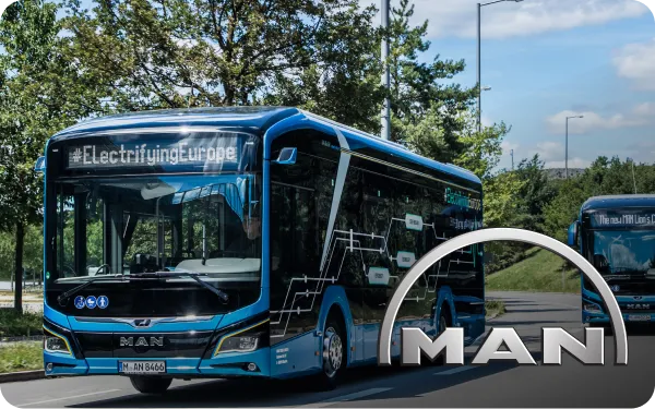 Blue MAN electric bus driving on a road, displaying "#ElectrifyingEurope" on its front, with trees and another bus in the background.