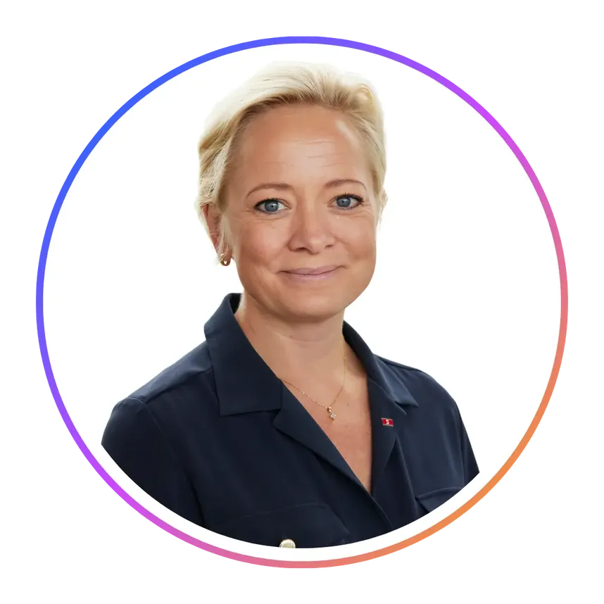 Smiling person with short blonde hair wearing a navy blouse, inside a circular frame with a colorful border on a white background.