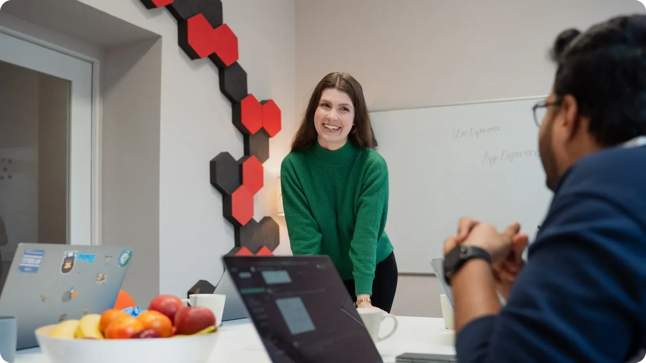 Staffbase employee in a green sweater smiling during a meeting near a whiteboard labeled "User Experience" and "App Experience."