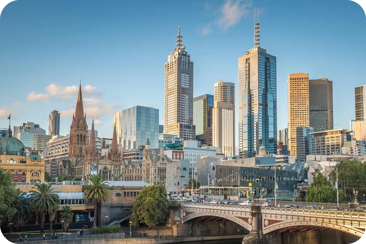Skyline of a city with modern skyscrapers, historic buildings, and a bridge over a river, set against a clear blue sky.
