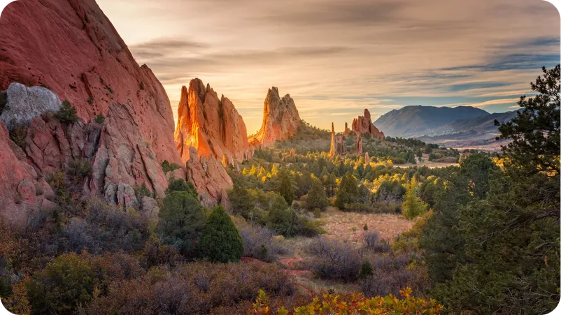 Red rock formations at Garden of the Gods in Colorado Springs, glowing at sunset with mountains in the distance.