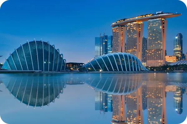 Skyline of Singapore at dusk, featuring Marina Bay Sands and futuristic domes, reflected in calm water under a clear blue sky.