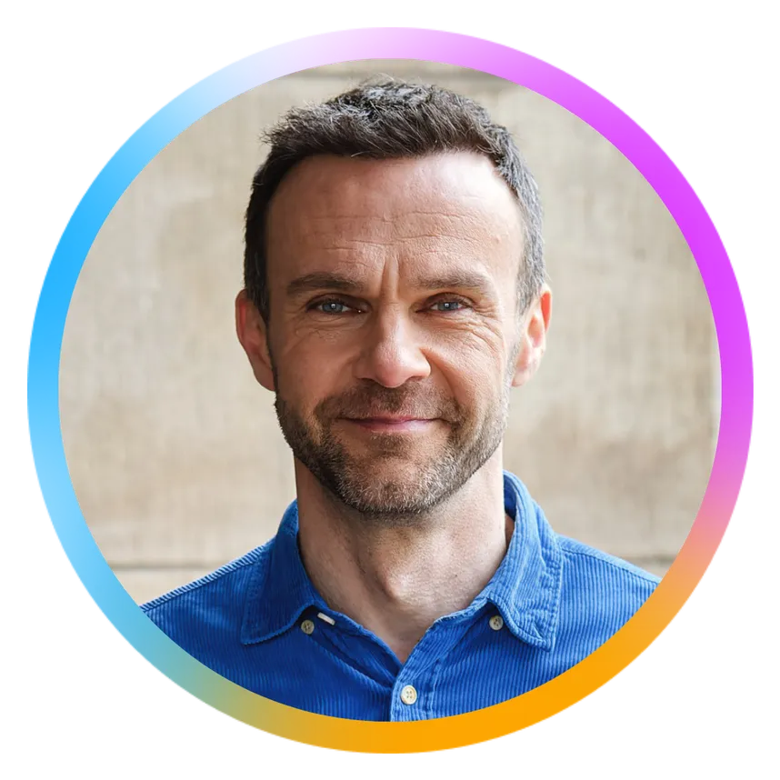 Smiling man with short hair and a beard wearing a blue shirt, framed by a colorful circular border.