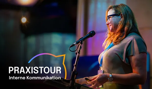 Woman speaking at a podium with a microphone, wearing glasses. "COMMS CLUB" text with colorful outline is visible on the left.