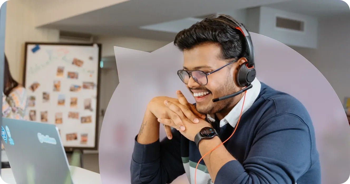 Staffbase employee smiling while on a call with a headset, sitting at his laptop. Title: Staffbase Sales Team Hero, Employee on Call