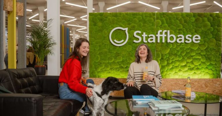 two women smile and laugh in front of Staffbase sign, dog in image