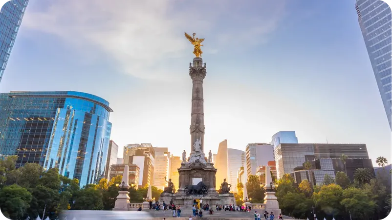 The Angel of Independence monument in Mexico City surrounded by modern skyscrapers at sunset.