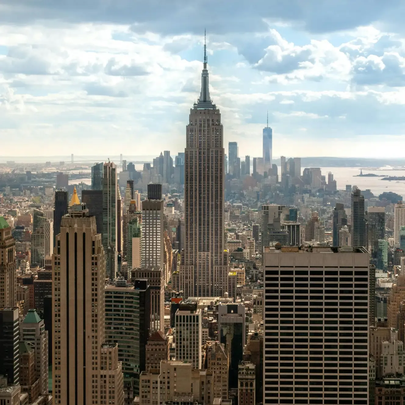 New York City skyline featuring the Empire State Building and One World Trade Center under a cloudy sky.