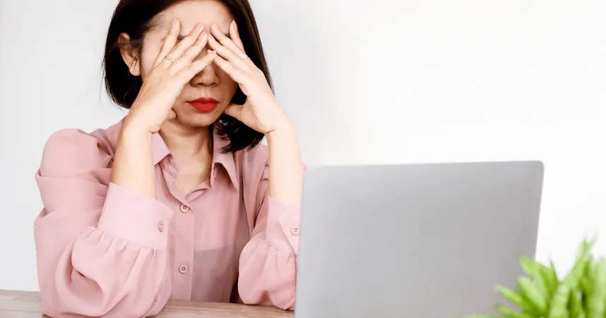 woman covers face while facing a laptop, image of apparent frustration