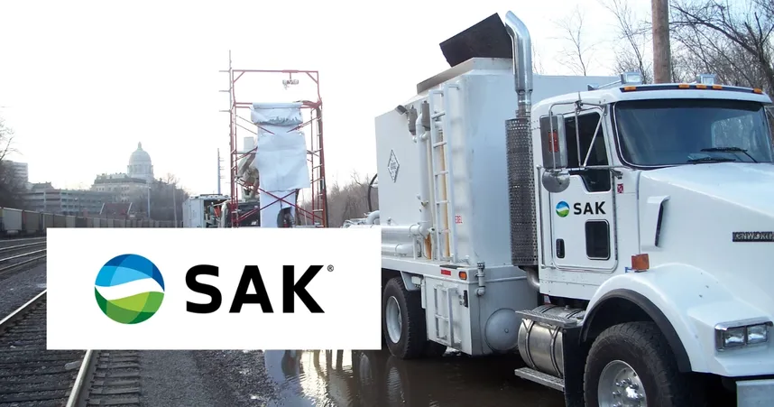SAK-branded truck near a construction site with scaffolding by railroad tracks; the Capitol building is visible in the background.