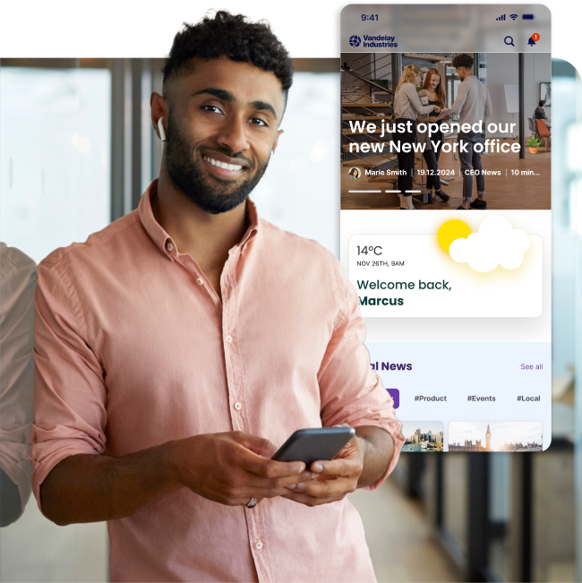 Smiling man in a pink shirt holds a phone. Nearby, a digital screen displays news about a new office opening and weather information.