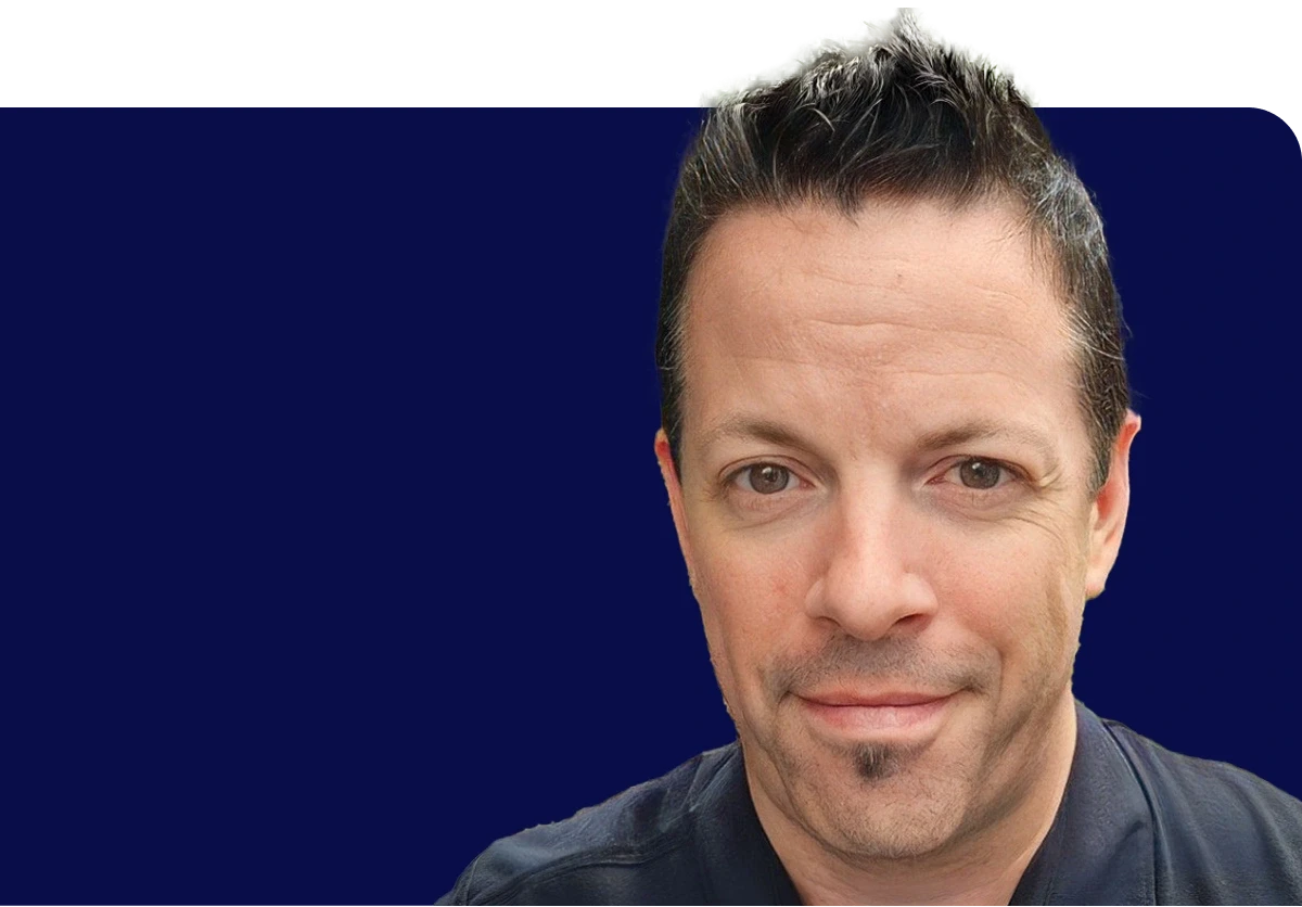 Man with short dark hair and a goatee, wearing a black shirt, against a solid dark blue background.