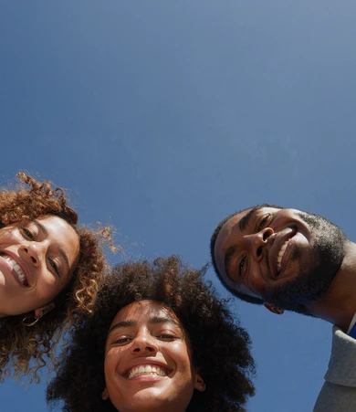 Three people smiling and looking down at the camera against a clear blue sky background.