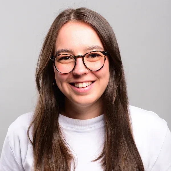 Headshot of Emily Heinrich. She is smiling into the camera. She wears a white shirt and glasses.