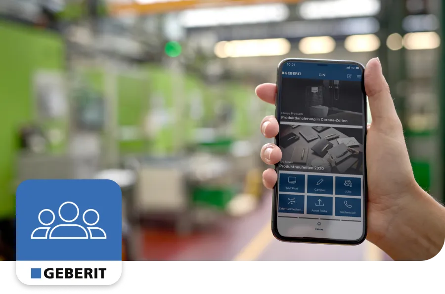 Hand holding a smartphone displaying the Geberit app in a modern industrial setting, with green machinery in the background.