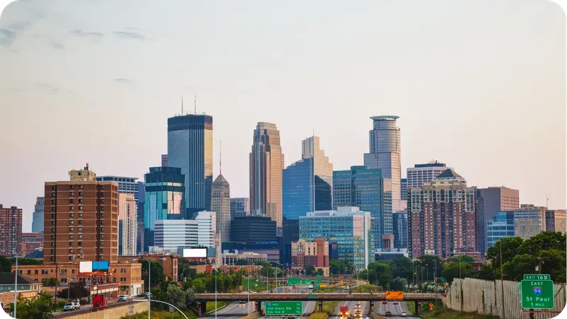 Minneapolis skyline at dusk with downtown highrises and highway signage for St. Paul.