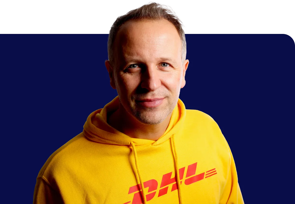 Man in a yellow DHL hoodie smiles against a dark blue background.
