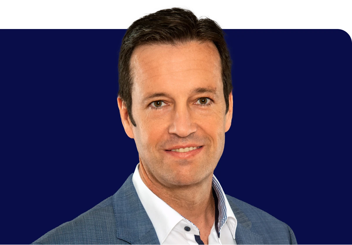 Smiling man in a blue suit jacket and white shirt against a dark blue background.