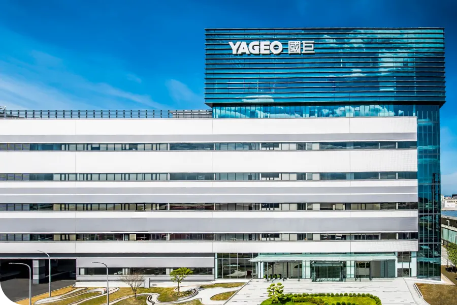 Modern multi-story building with "YAGEO" logo on top, glass facade, and landscaped surroundings under a clear blue sky.