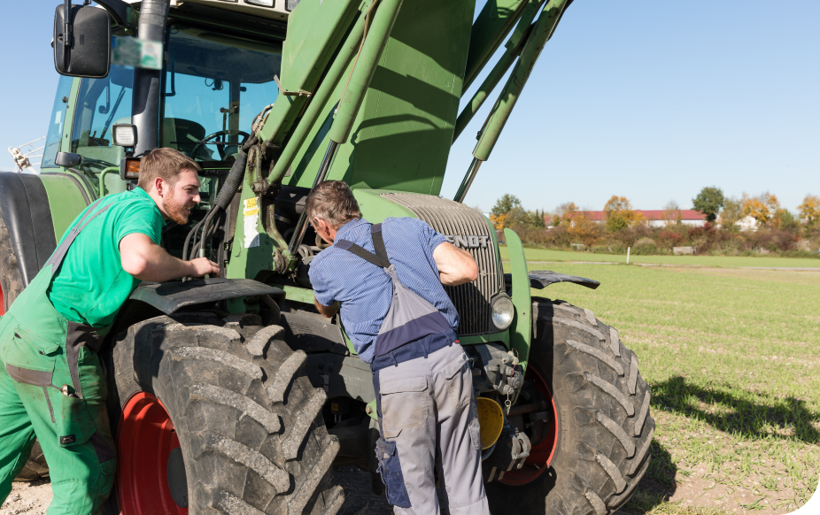 Two men in work clothes inspecting a green tractor in a field under a clear blue sky.