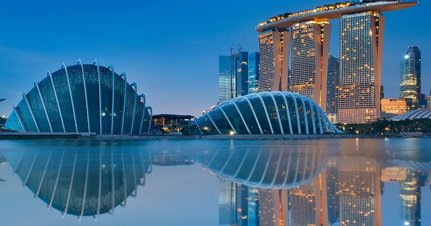 Skyline of Singapore at dusk, featuring Marina Bay Sands and futuristic domes, reflected in calm water under a clear blue sky.