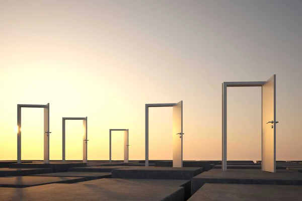 Five open doors standing on a flat surface, silhouetted against a warm, glowing sunset sky.