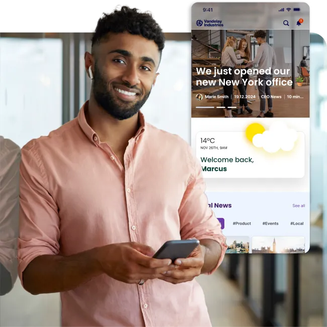 Smiling man in a pink shirt holds a phone. Nearby, a digital screen displays news about a new office opening and weather information.