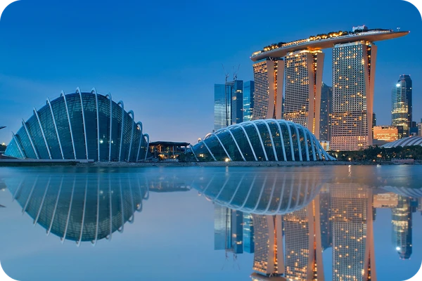 Skyline of Singapore at dusk, featuring Marina Bay Sands and futuristic domes, reflected in calm water under a clear blue sky.