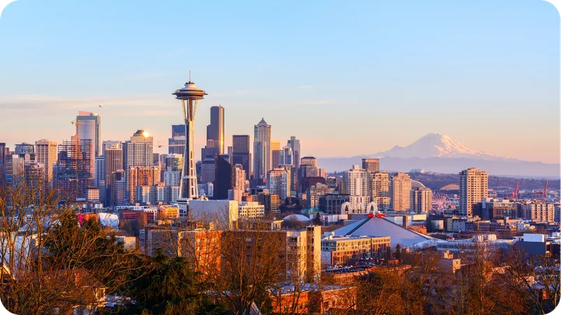 Seattle skyline at sunset featuring the Space Needle with Mount Rainier visible in the distance.
