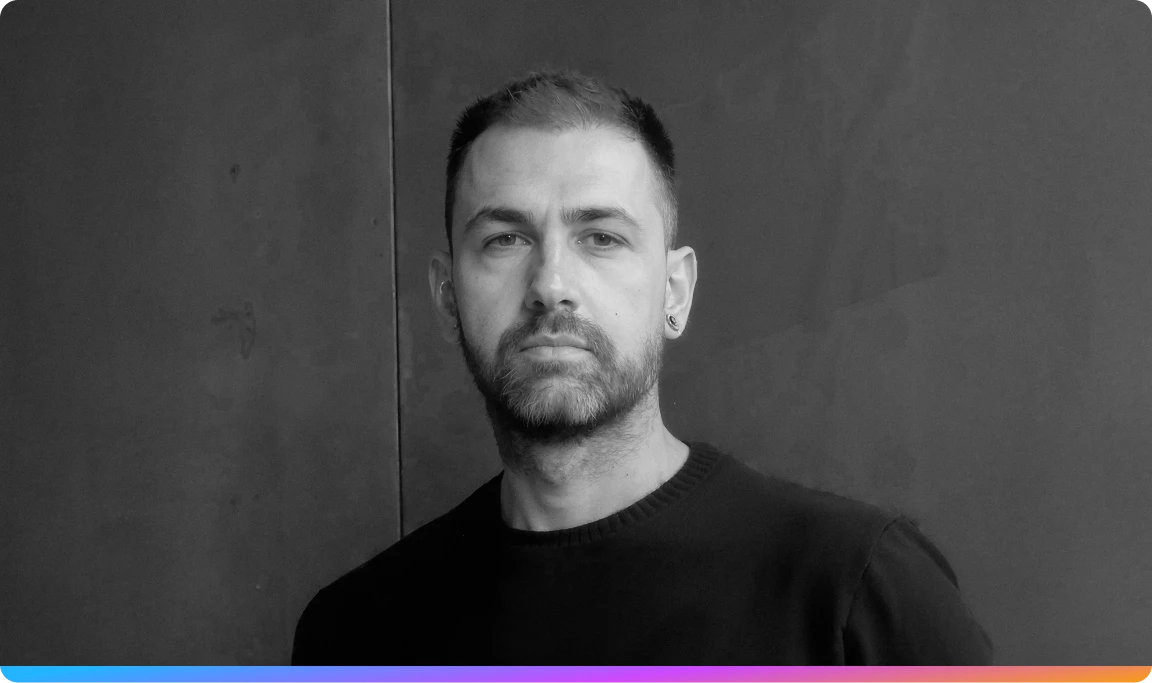 Black and white portrait of Giovanni Luperti with short hair and a beard, wearing a dark sweater, standing against a textured wall.