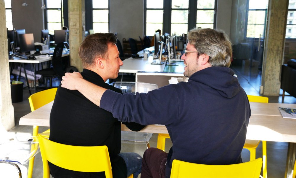 two men embrace each other in a friendly manner in an office setting