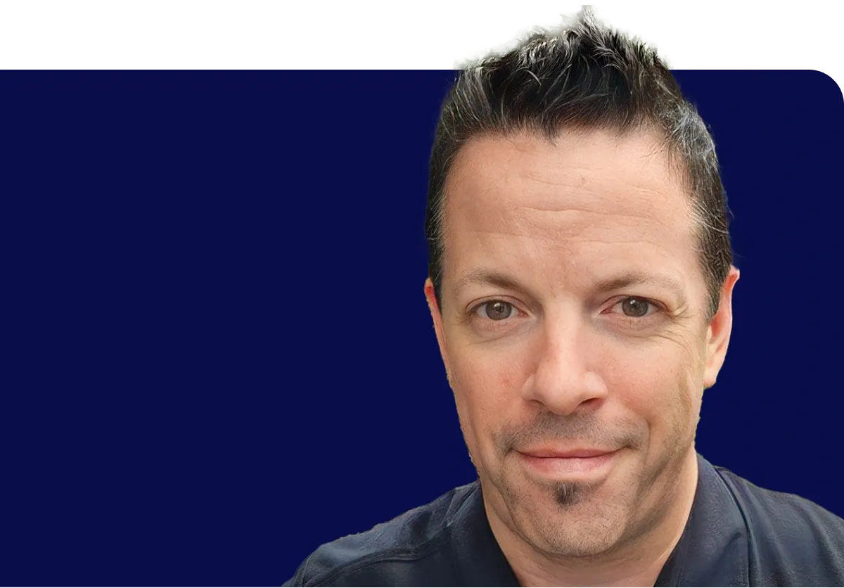 Man with short dark hair and a goatee, wearing a black shirt, against a solid dark blue background.
