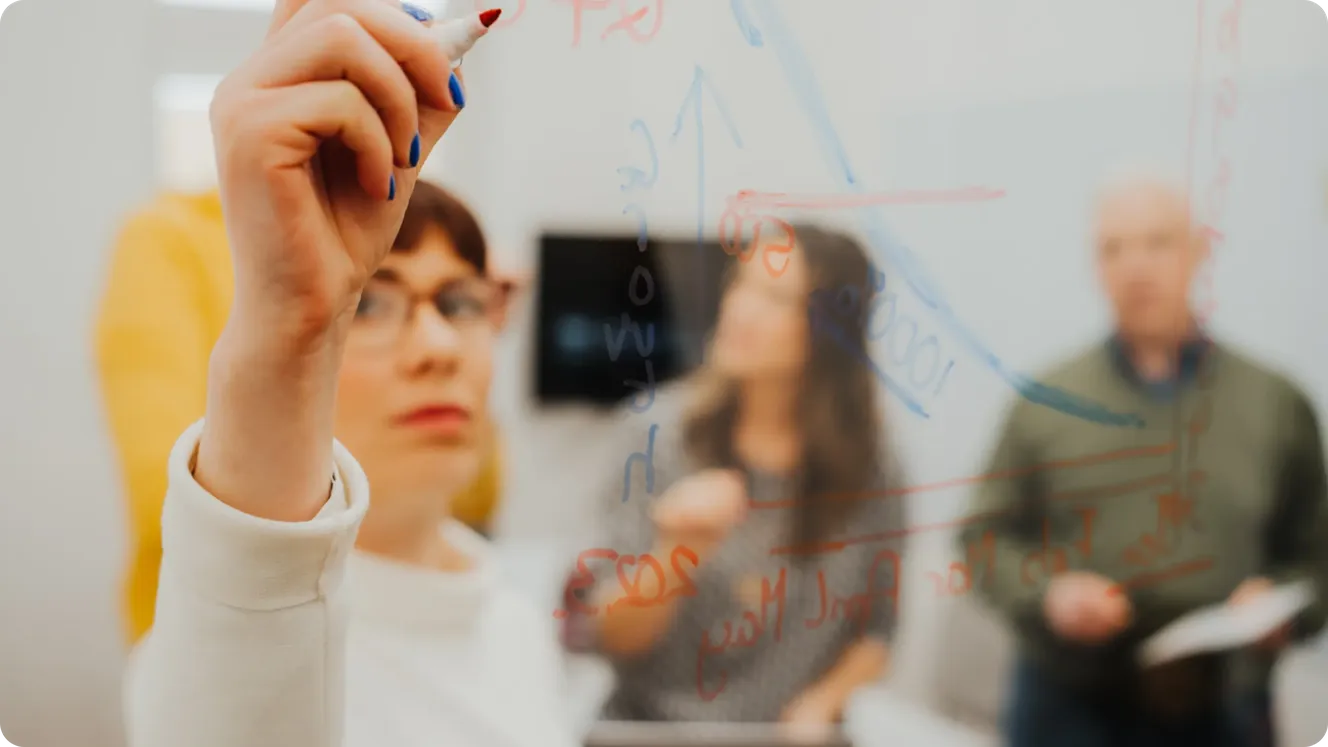 taffbase employee writing growth projections on a glass board while colleagues look on.