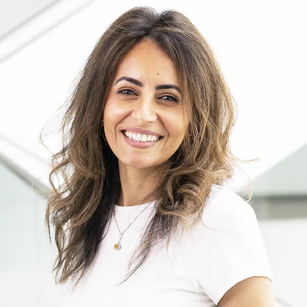 Darin Gad smiling in a white shirt, standing in a bright, modern indoor space with glass railings.