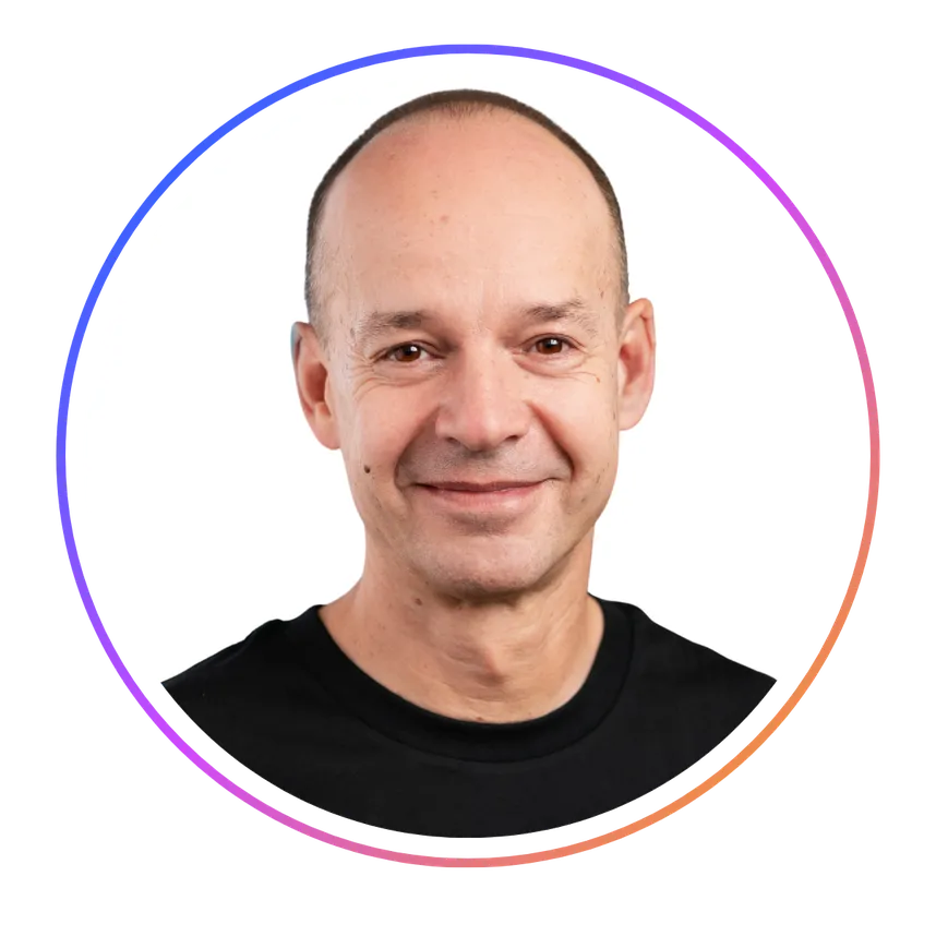 Smiling person with a shaved head wearing a black shirt, framed in a circular border with a gradient color.