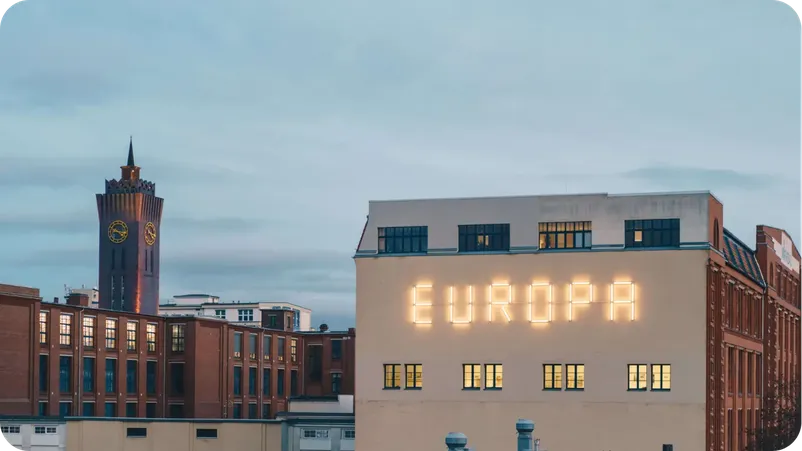 Chemnitz skyline at dusk with a historic clock tower and an illuminated "EUROPA" sign on a building facade.