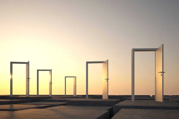 Five open doors standing on a flat surface, silhouetted against a warm, glowing sunset sky.