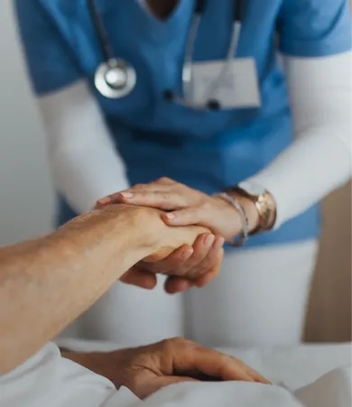 Nurse in blue scrubs gently holding an elderly patient's hand, providing comfort and care in a medical setting.