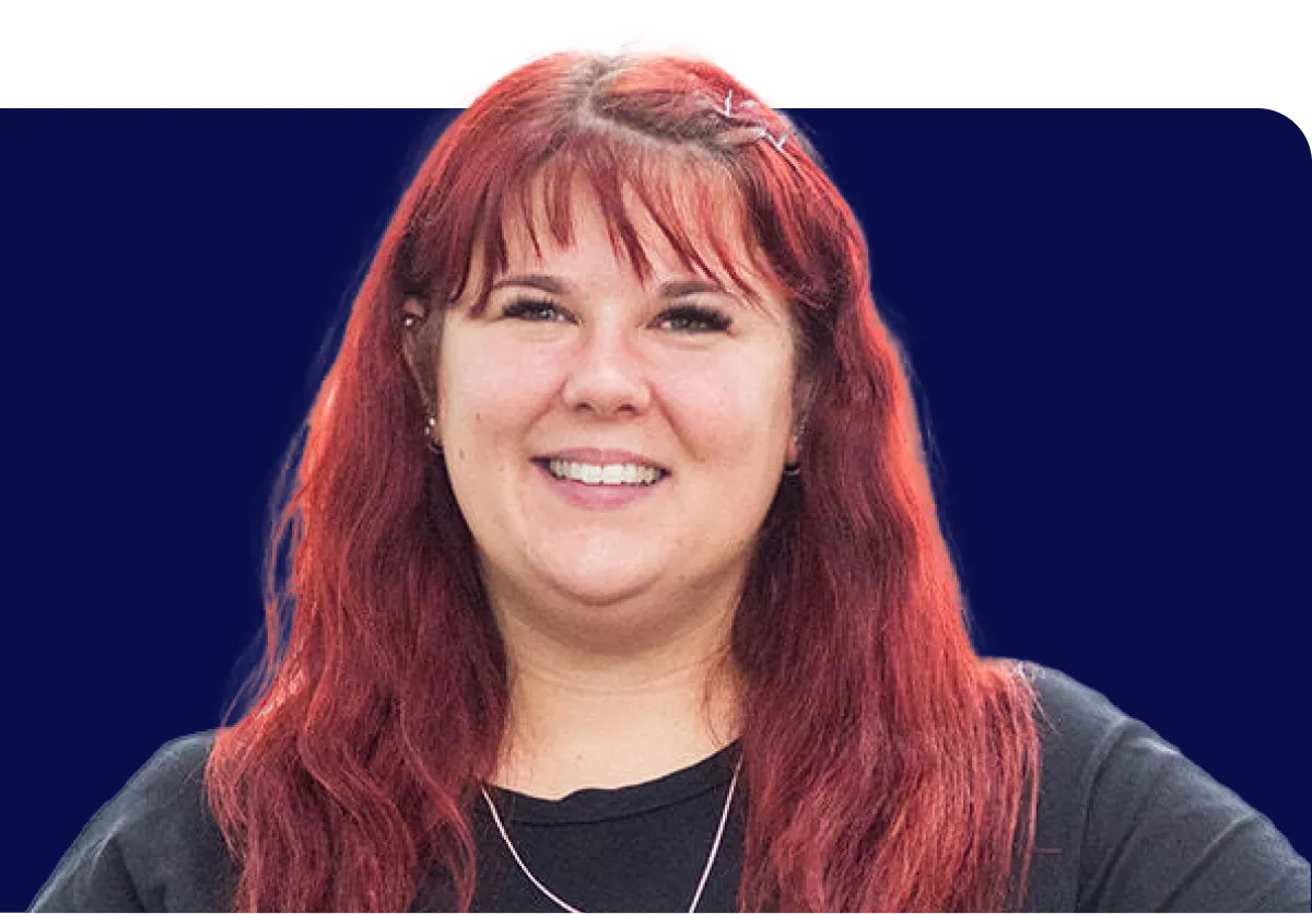 Smiling person with long red hair, wearing a black shirt and necklace, against a dark blue background.