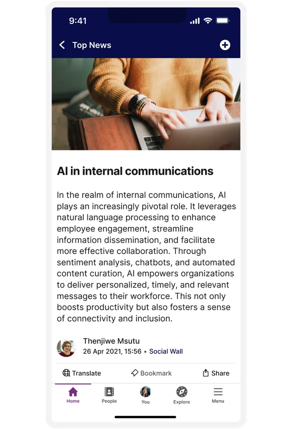 A person using a laptop, with an article on AI in internal communications displayed on a smartphone screen.
