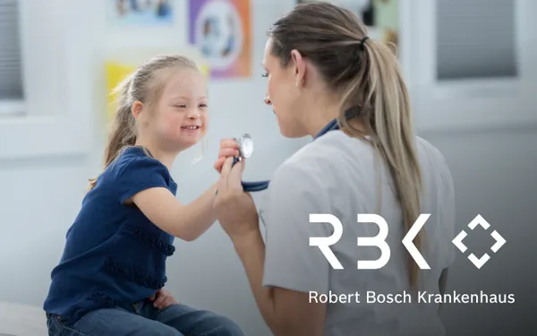A doctor smiles while examining a child with a stethoscope in a medical setting. Robert Bosch Krankenhaus logo in the foreground.