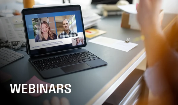 Laptop on a desk showing a webinar with two smiling speakers. The screen displays "WEBINARS" in bold text.