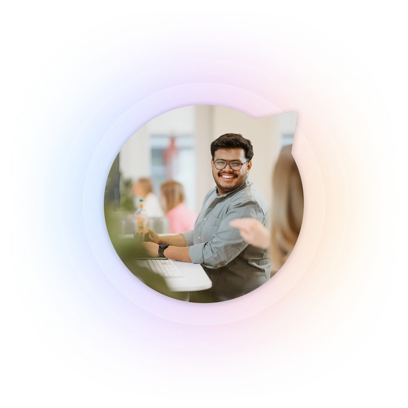 Staffbase employee smiling and gesturing at his desk during a conversation with a colleague.
