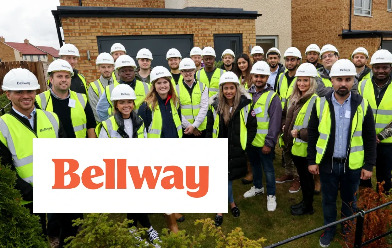 Bellway logo over photo of a large group of employees in hard hats and hi-vis vests standing together outside a housing development.