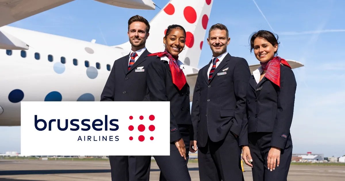 Brussels Airlines crew in uniform stand in front of an airplane with a red and blue dotted tail, smiling under a clear sky.