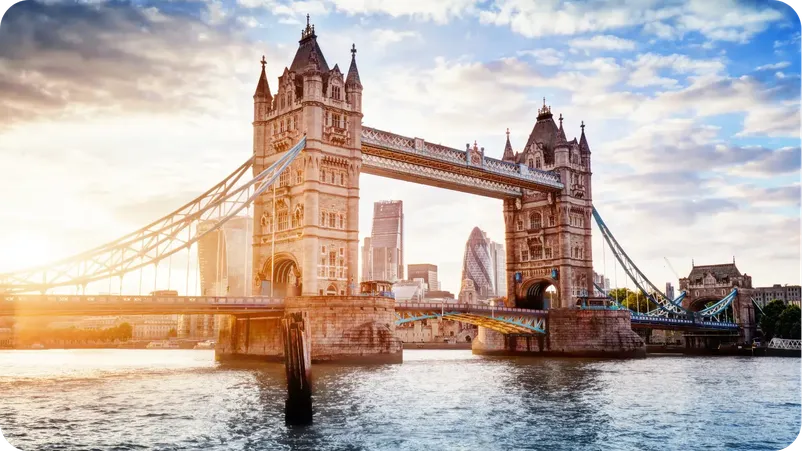 Tower Bridge in London at sunrise, with the City of London skyline visible between the towers.