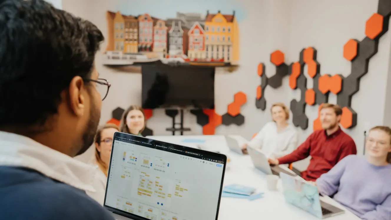 Staffbase colleagues in a meeting room discussing a Miro board displayed on a laptop and screen.