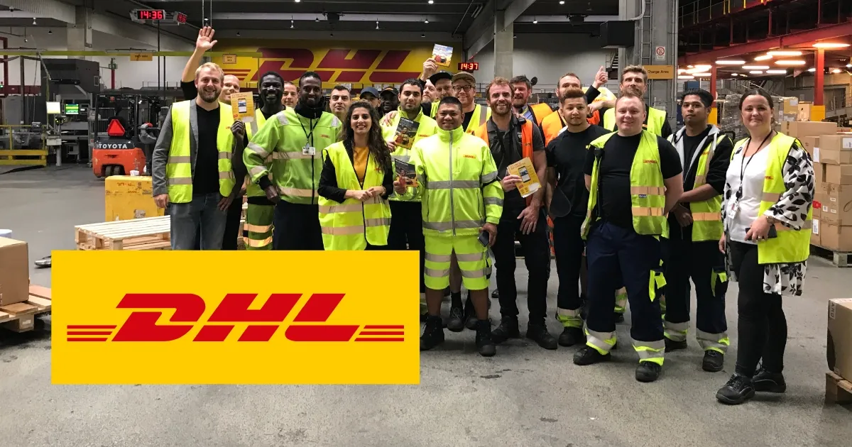 A group of DHL employees in high-visibility clothing smiling and posing in a warehouse, with DHL logo prominently displayed.