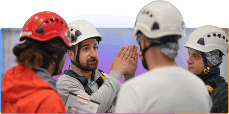 Group of industrial workers wearing helmets and safety gear, with one man using hand gestures to explain something during a discussion.
